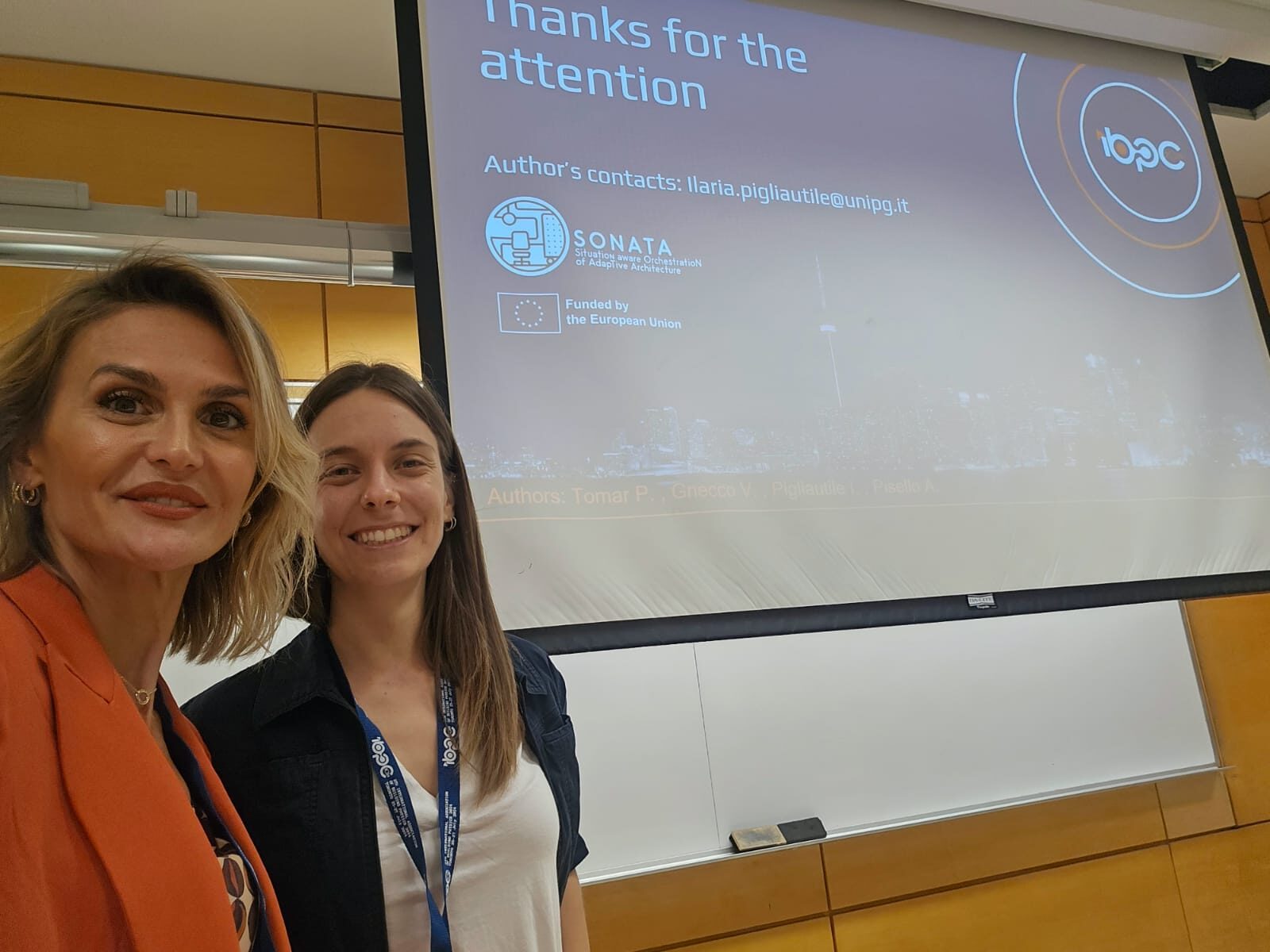 Two women stand in front of a presentation screen showing a SONATA presentation slide