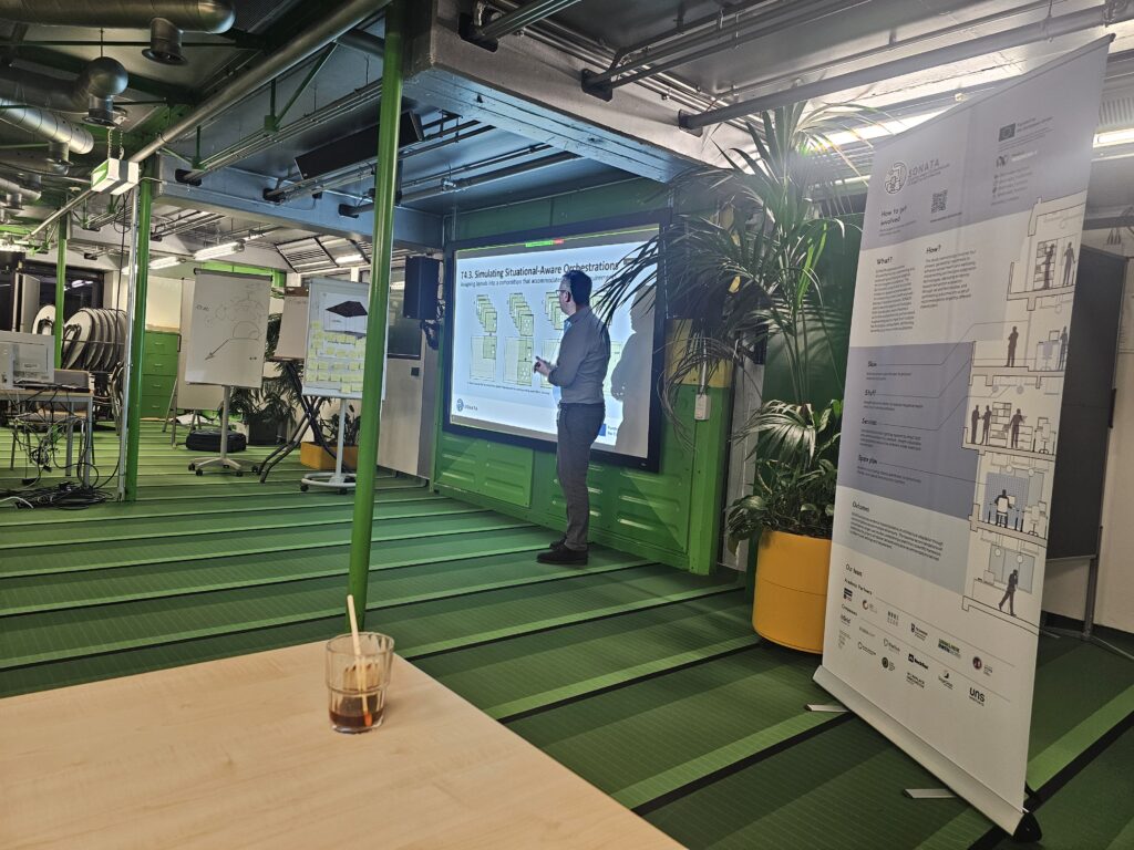 Man stands in front of presentation screen, presenting (text on slide illegible) in a green meeting room.
