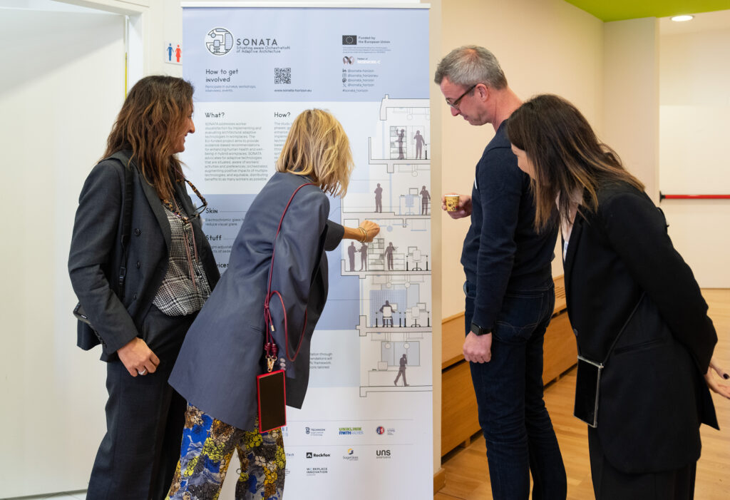 Four people stand in an office, attentively reading a poster titled "Sonata." They appear engaged, discussing the content about community involvement.